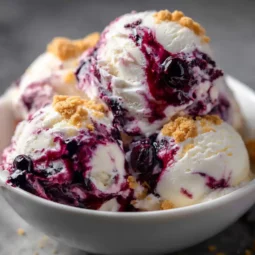 three scoops of blueberry cheesecake ice cream in a bowl with blueberry swirl and graham cracker crumbs