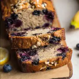 Slices of lemon blueberry banana bread on parchment with blueberries and lemon