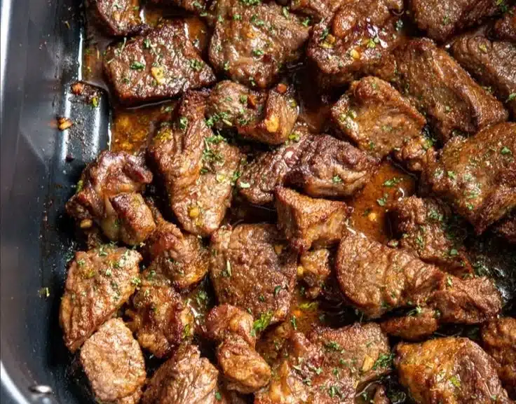 Garlic butter steak bites served on a plate with herbs and seasonings.