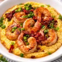 A bowl of southern shrimp and grits topped with shrimp, creamy cheese, and gravy.